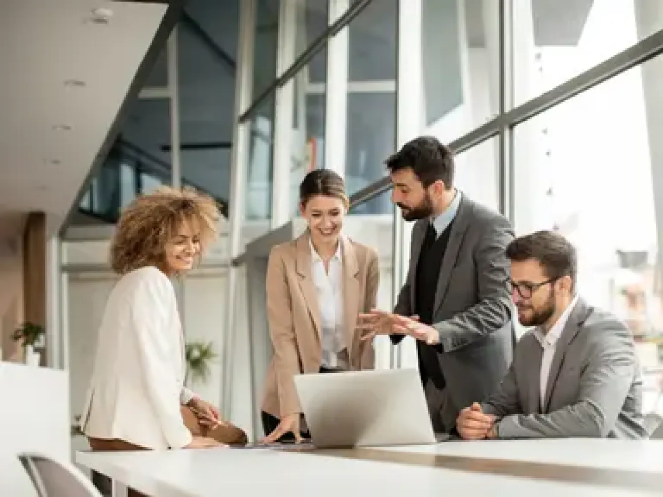 a man a woman standing up a second woman is sitting on a desk and an other man sitting on a chair all of them around a laptop