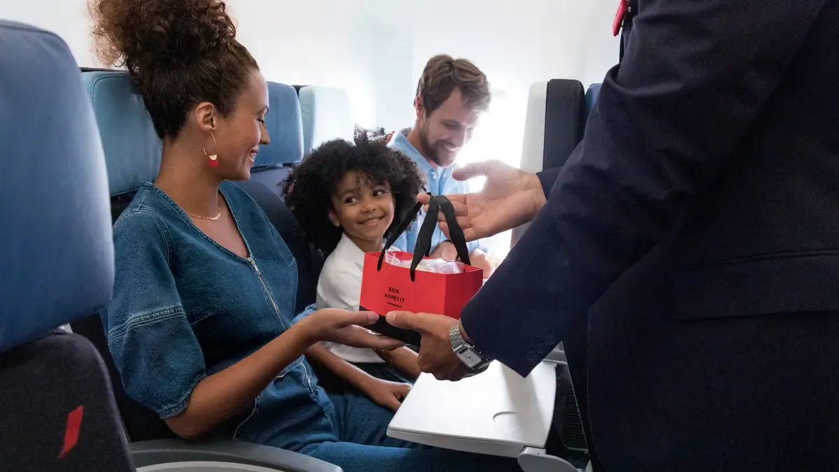 flight attendant giving a gift to to aw woman, the mona is looking with a smile to her kid whom is smiling too. all on board of a plan